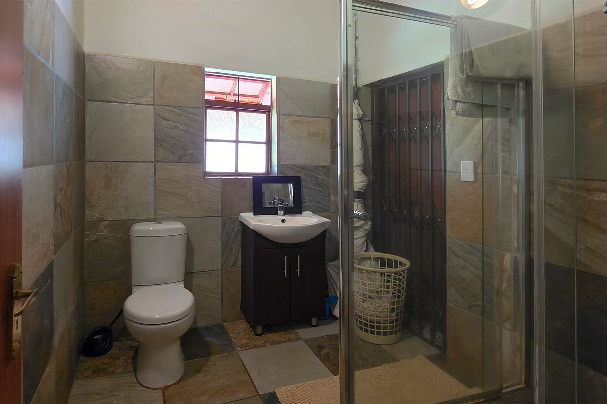 A functional bathroom featuring a shower enclosure, vanity basin, and toilet, finished with natural stone-look wall and floor tiles.