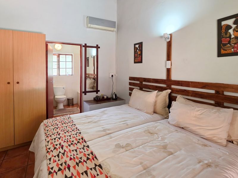 A functional bedroom featuring tiled flooring, a built-in wardrobe, split-system air conditioning, and an adjoining en-suite bathroom.