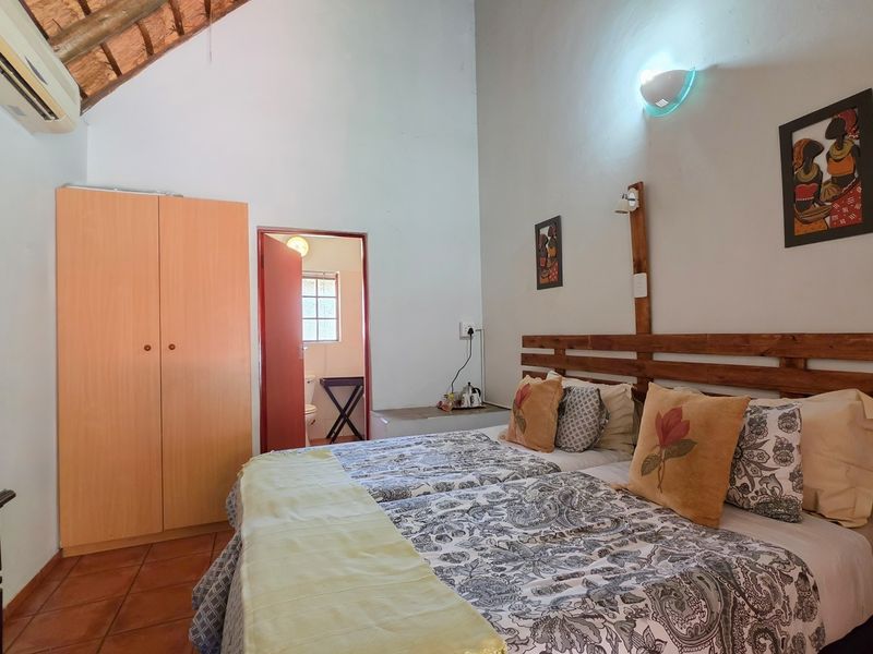 A bedroom featuring tiled flooring, an exposed thatch ceiling, built-in wardrobe, and an en-suite bathroom access.
