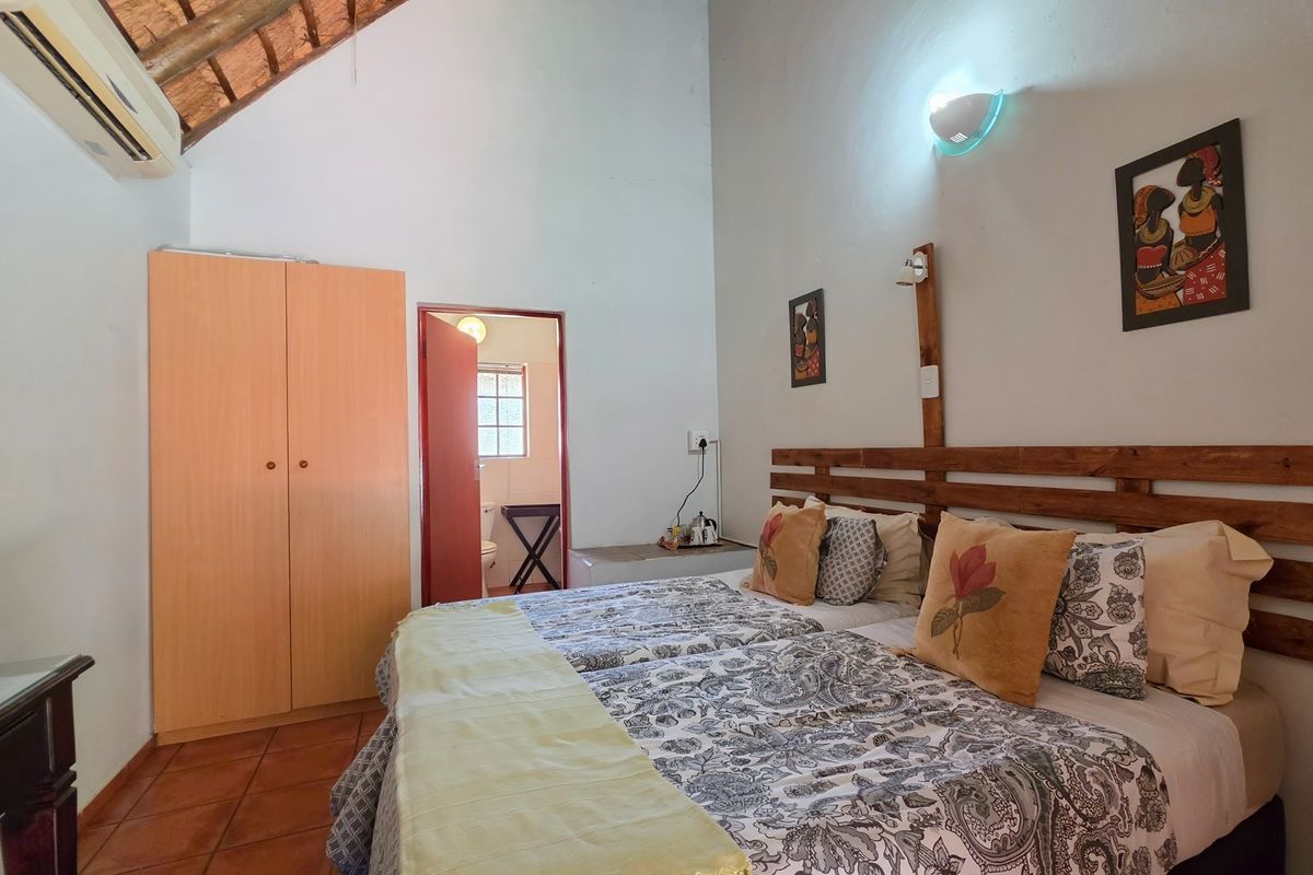 A bedroom featuring tiled flooring, an exposed thatch ceiling, built-in wardrobe, and an en-suite bathroom access.