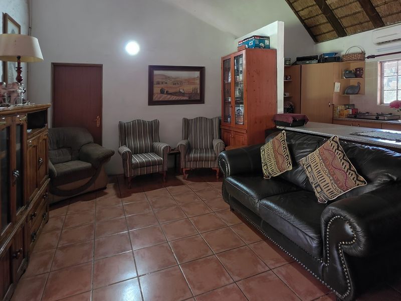 Open-plan living area featuring tiled floors, a vaulted ceiling with exposed thatch, and an integrated kitchen space with air conditioning.