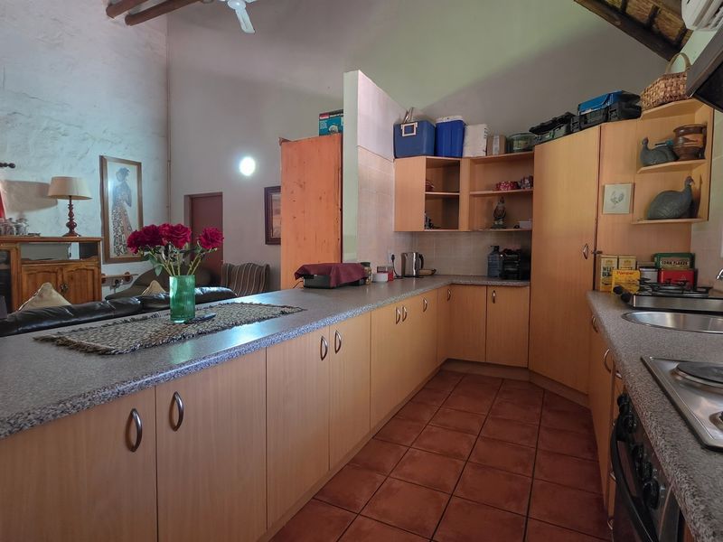 Open-plan kitchen featuring wooden cabinetry, laminate countertops, and tiled flooring, seamlessly integrated with the living area under a high vaulted ceiling with exposed rafters.