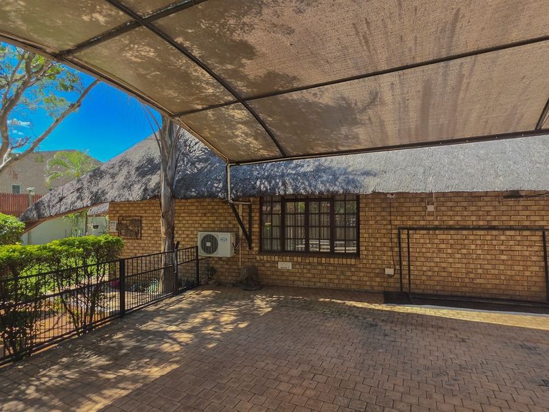 A covered outdoor patio area featuring a thatch roof, brick exterior walls, and paved flooring, providing a functional space for outdoor living.