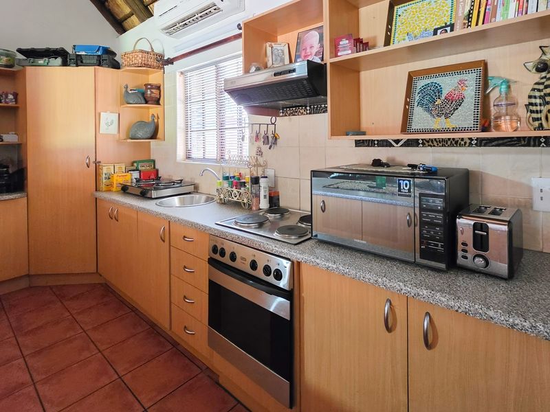 A functional kitchen featuring light wood cabinetry, granite countertops, a built-in oven with electric hob, and tiled flooring.
