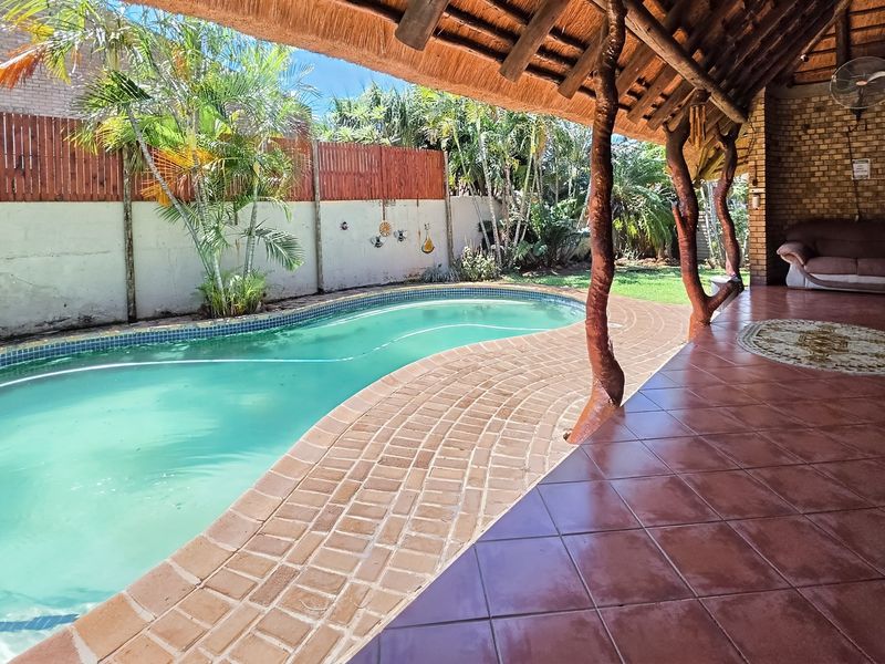 Outdoor entertainment area featuring a covered thatched patio, tiled flooring, and a swimming pool set within a private garden with boundary walls.