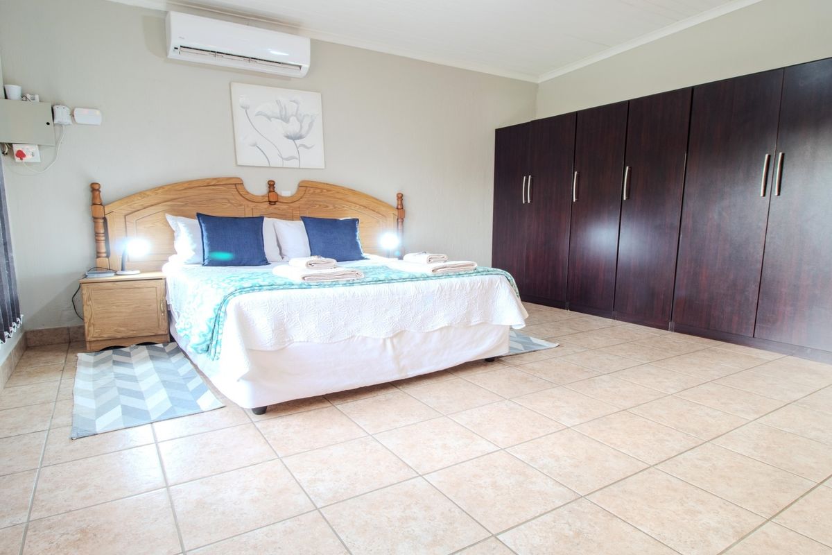Spacious bedroom featuring large dark wood built-in cupboards, tiled flooring, and a wall-mounted air conditioning unit.
