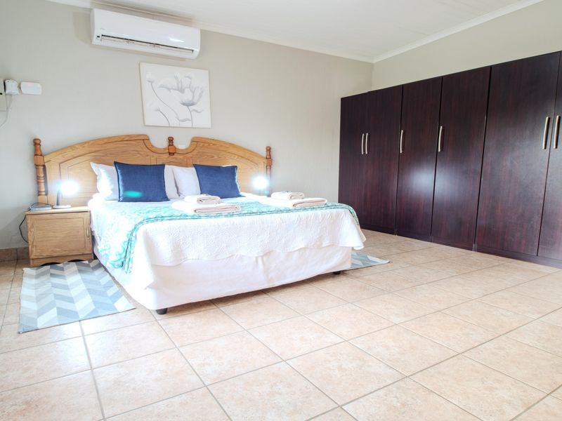 Spacious bedroom featuring large dark wood built-in cupboards, tiled flooring, and a wall-mounted air conditioning unit.