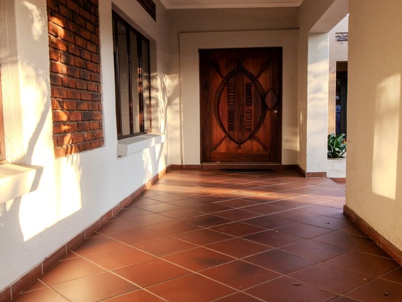 A covered entrance porch featuring terracotta floor tiles, a solid wood front door, and an exposed brick feature wall.