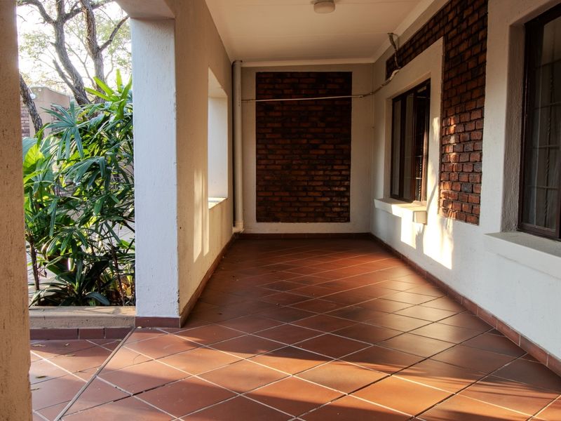 A covered outdoor patio featuring terracotta tiled flooring, an exposed brick feature wall, and structural columns, offering a functional space for outdoor living.