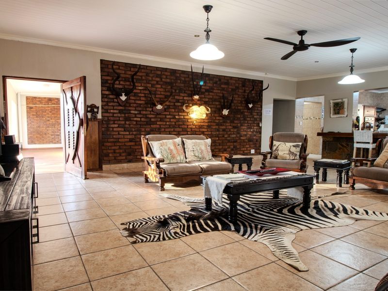 Spacious open-plan living area featuring a prominent exposed brick wall, tiled flooring, and a classic tongue and groove ceiling with integrated lighting.