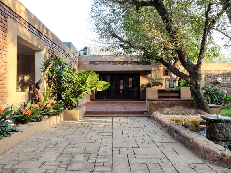 A well-maintained rear exterior featuring a paved patio, brick wall construction, and a decorative water feature set within a landscaped garden area.
