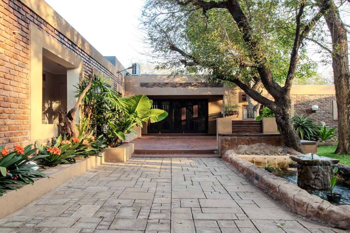 A well-maintained rear exterior featuring a paved patio, brick wall construction, and a decorative water feature set within a landscaped garden area.