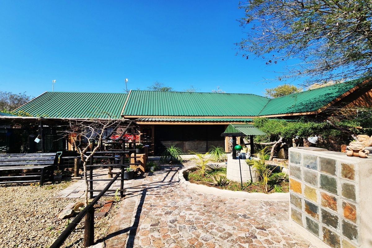 Rear exterior view of the property featuring a green metal roof, stone paved walkway, and a decorative stone well in the garden area.