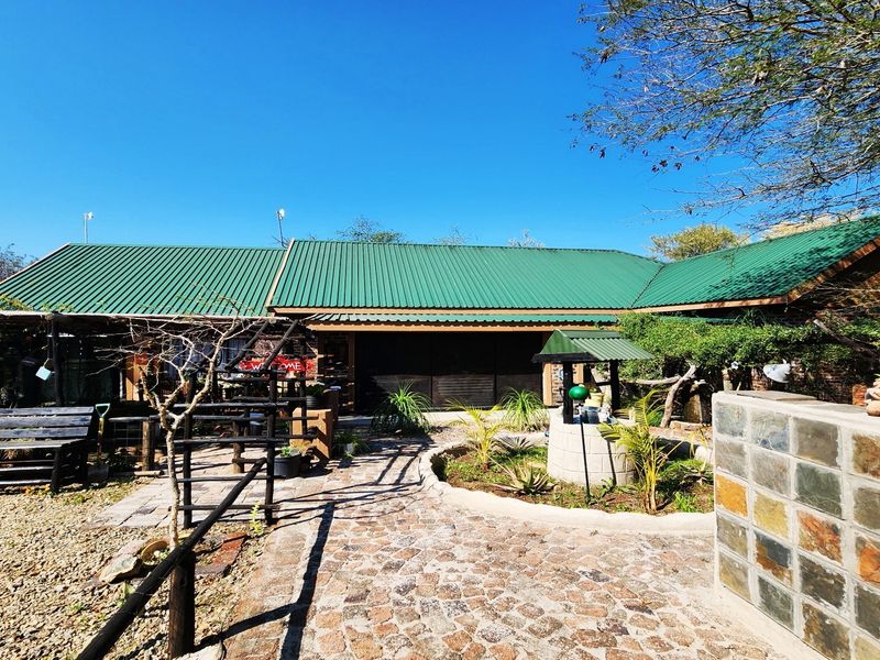 Rear exterior view of the property featuring a green metal roof, stone paved walkway, and a decorative stone well in the garden area.