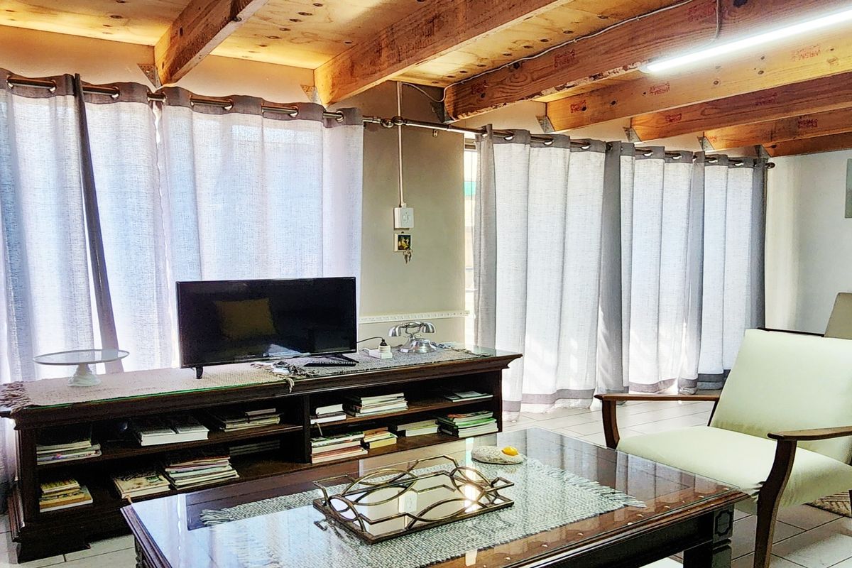 Living room featuring exposed timber ceiling beams, tiled flooring, and large sliding glass doors providing ample natural light.