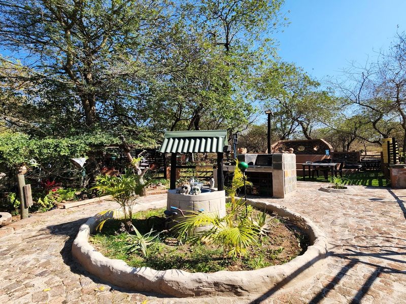 Outdoor garden area featuring a stone-paved patio, a built-in brick braai, and a decorative stone well set within a landscaped circular garden bed.