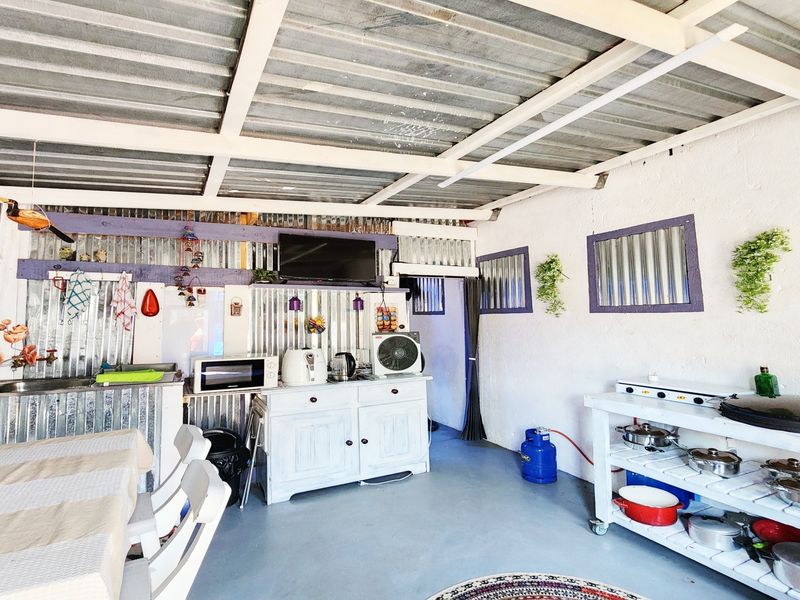 A covered outdoor patio area featuring corrugated metal roofing and wall cladding, providing a functional space for outdoor dining and food preparation.
