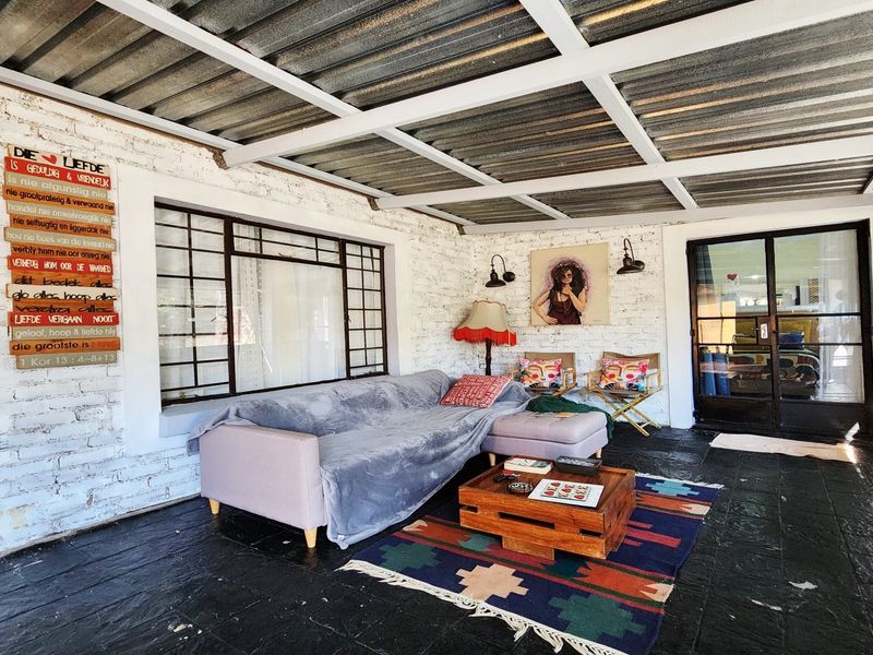 Covered patio area featuring exposed beam ceiling, painted brick walls, and dark stone tile flooring, providing a versatile outdoor living space.