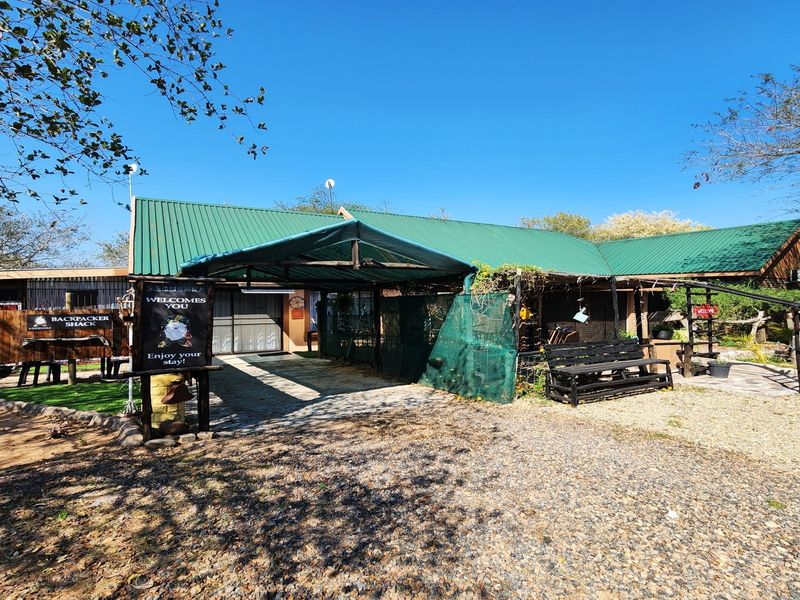 Front exterior view of a rustic property featuring a corrugated metal roof, covered patio area, and gravel driveway access.