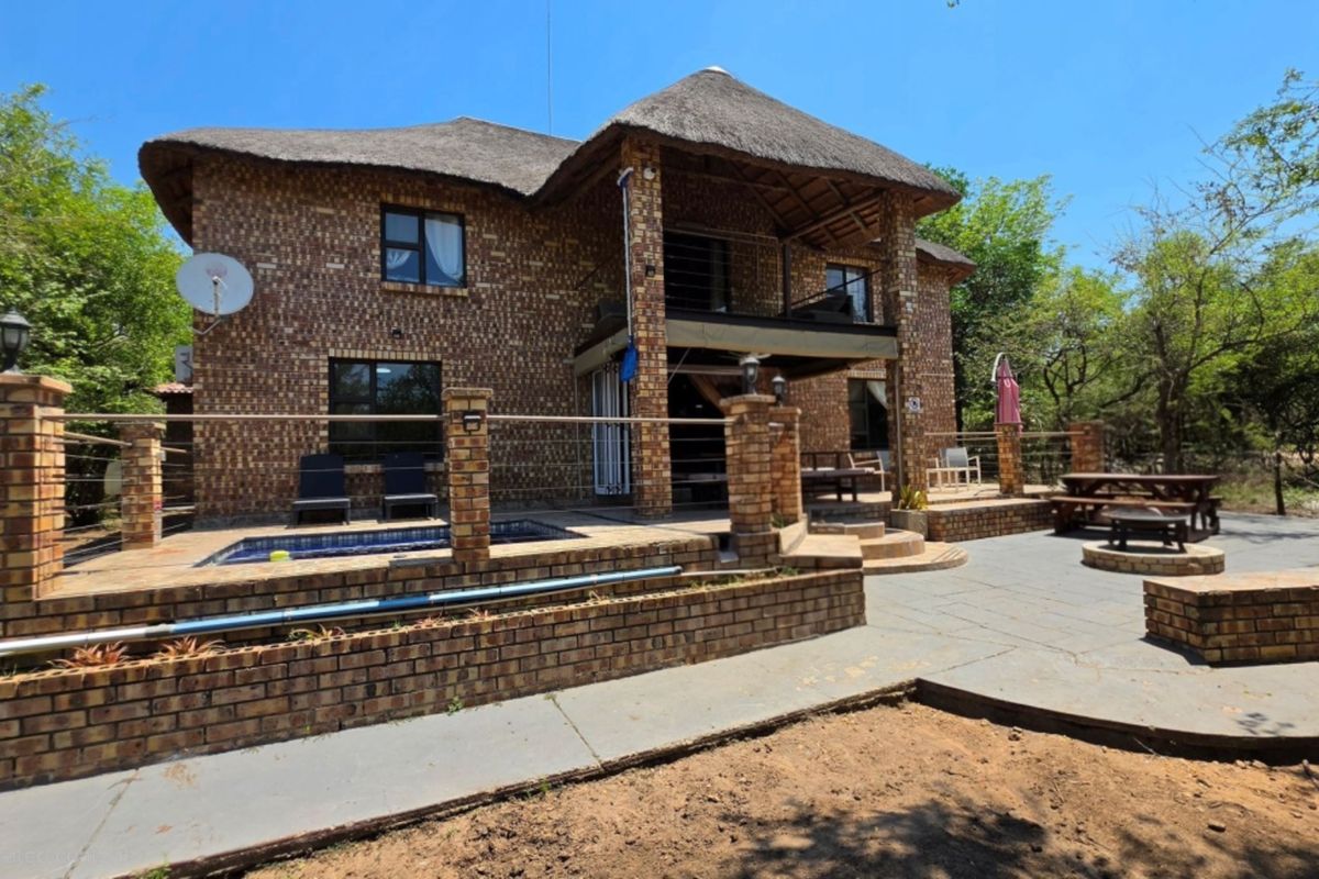 Rear view of a double-story face brick house featuring a thatched roof, swimming pool, paved patio area, and a balcony.