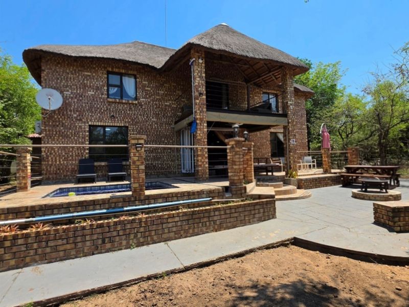 Rear view of a double-story face brick house featuring a thatched roof, swimming pool, paved patio area, and a balcony.