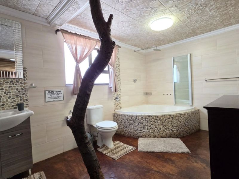 Spacious bathroom featuring a corner bathtub with pebble-tiled surround, vanity basin, and unique architectural elements including a central tree trunk feature.