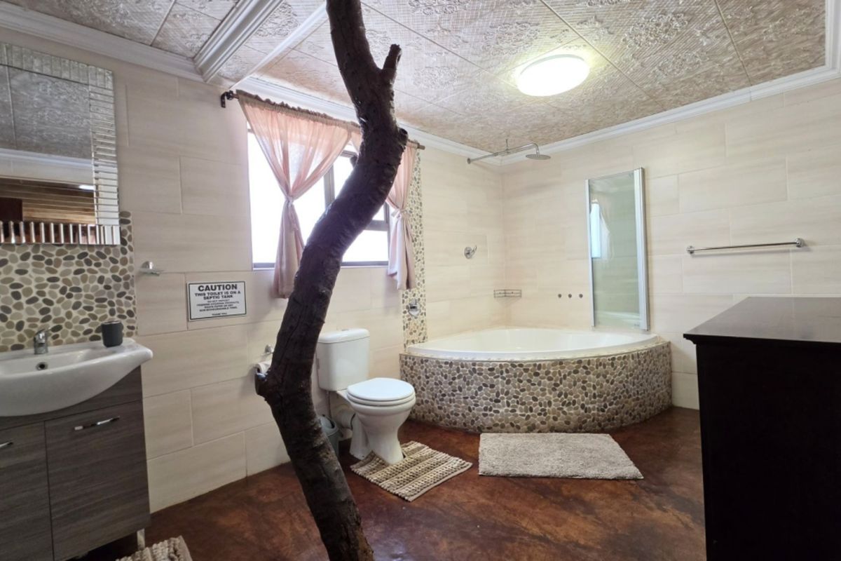 Spacious bathroom featuring a corner bathtub with pebble-tiled surround, vanity basin, and unique architectural elements including a central tree trunk feature.