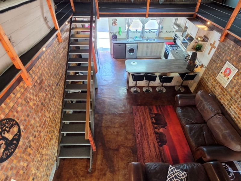 An open-plan living and kitchen area featuring exposed brick walls, a modern metal staircase leading to a mezzanine, and polished concrete flooring.