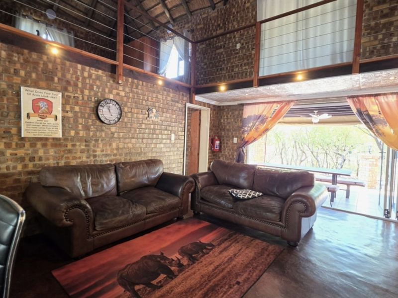 Spacious living area featuring exposed brick walls, a high thatch ceiling, and a mezzanine level, with direct access to an outdoor patio.