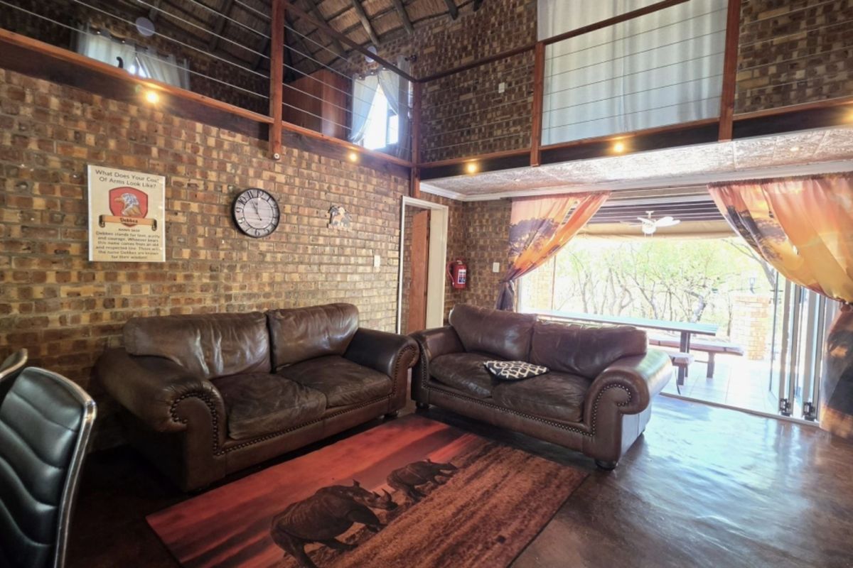 Spacious living area featuring exposed brick walls, a high thatch ceiling, and a mezzanine level, with direct access to an outdoor patio.