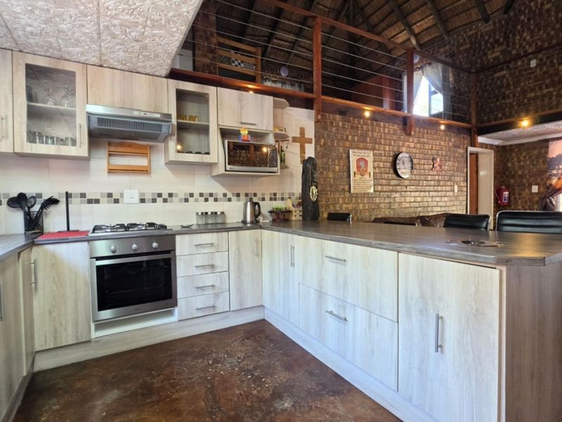 Open-plan kitchen featuring light wood cabinetry, built-in appliances, and a breakfast bar, set against a rustic exposed brick wall and mezzanine level.