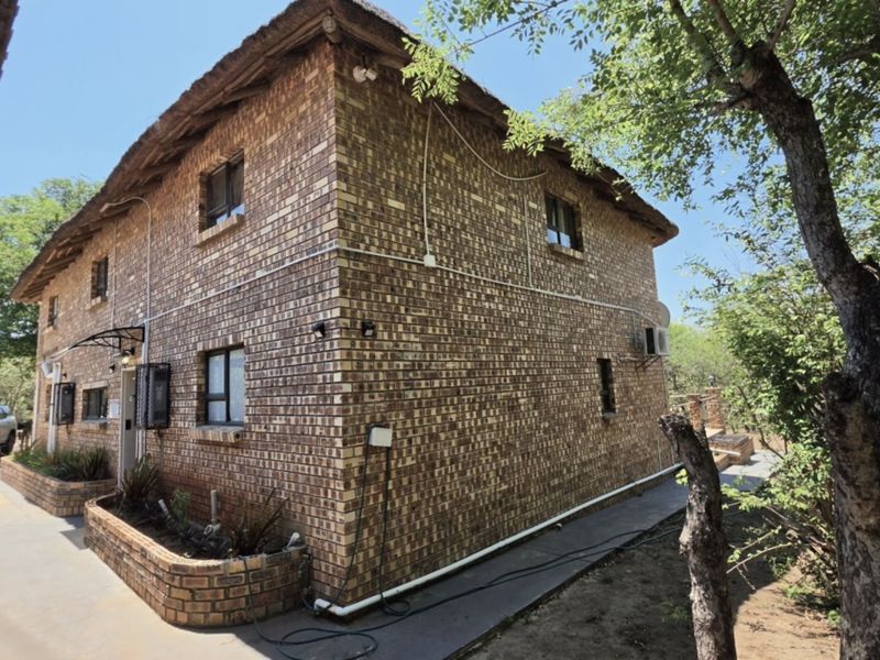 A two-story face brick house featuring a traditional thatch roof, external brick planter boxes, and secure aluminum-framed windows.