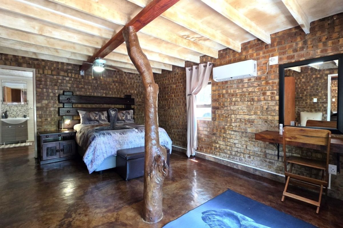 Spacious bedroom featuring rustic exposed brick walls, polished concrete floors, and exposed timber ceiling beams, complemented by a built-in vanity and air conditioning.
