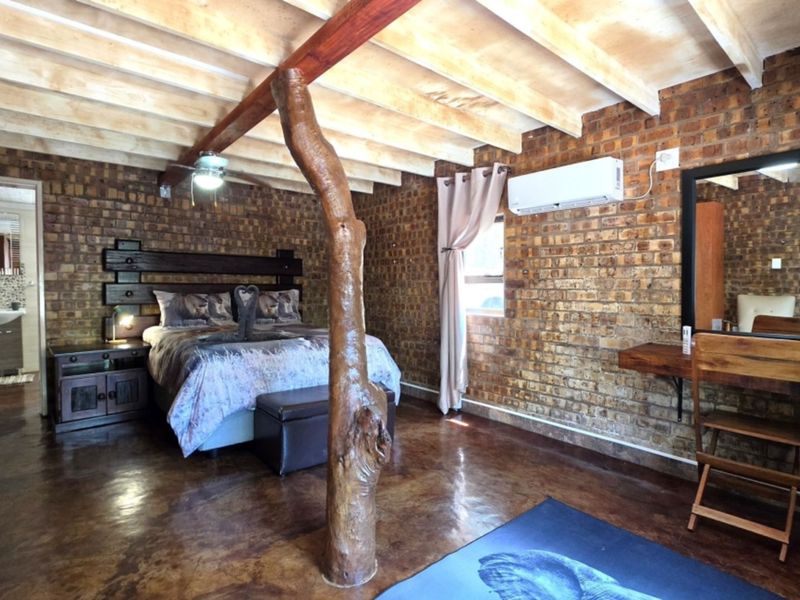 Spacious bedroom featuring rustic exposed brick walls, polished concrete floors, and exposed timber ceiling beams, complemented by a built-in vanity and air conditioning.