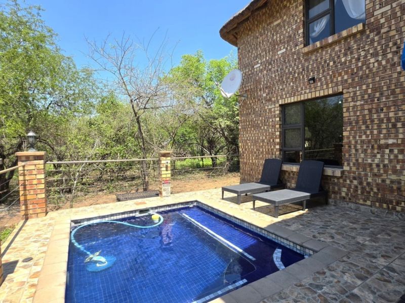 A private plunge pool area featuring stone paving, brick pillars, and a rustic brick facade, set against a natural bushveld backdrop.