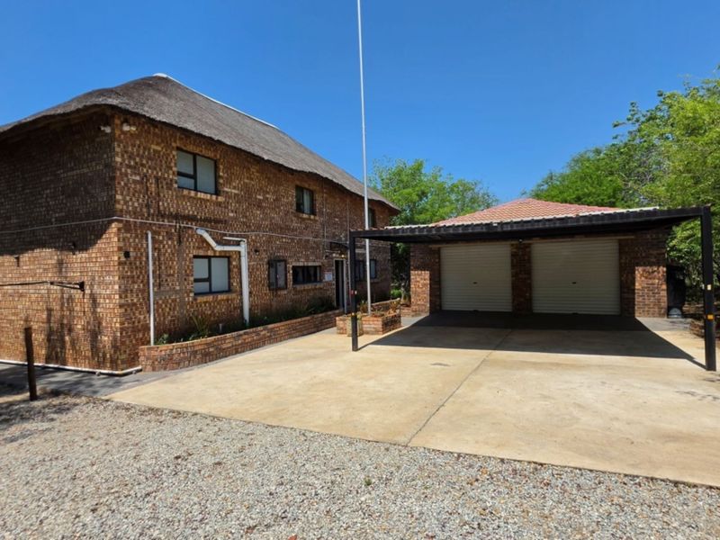 A double-story facebrick house featuring a traditional thatch roof and an attached double carport with roller doors.
