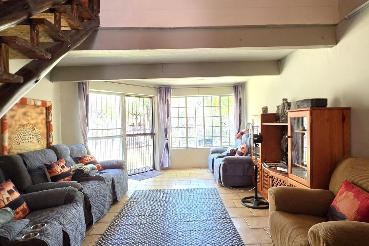 A living room featuring tiled flooring, exposed timber staircase, and natural light through steel-framed windows with security access.