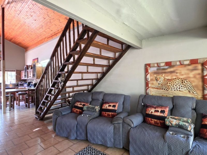Open plan living area featuring a timber staircase, exposed wood ceiling, and tiled flooring, seamlessly connecting to the kitchen space.
