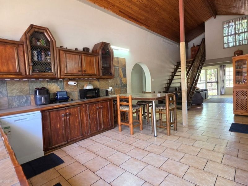 Open plan kitchen and living area featuring wooden cabinetry, stone tile backsplash, tiled flooring, and an exposed wooden ceiling with a staircase.