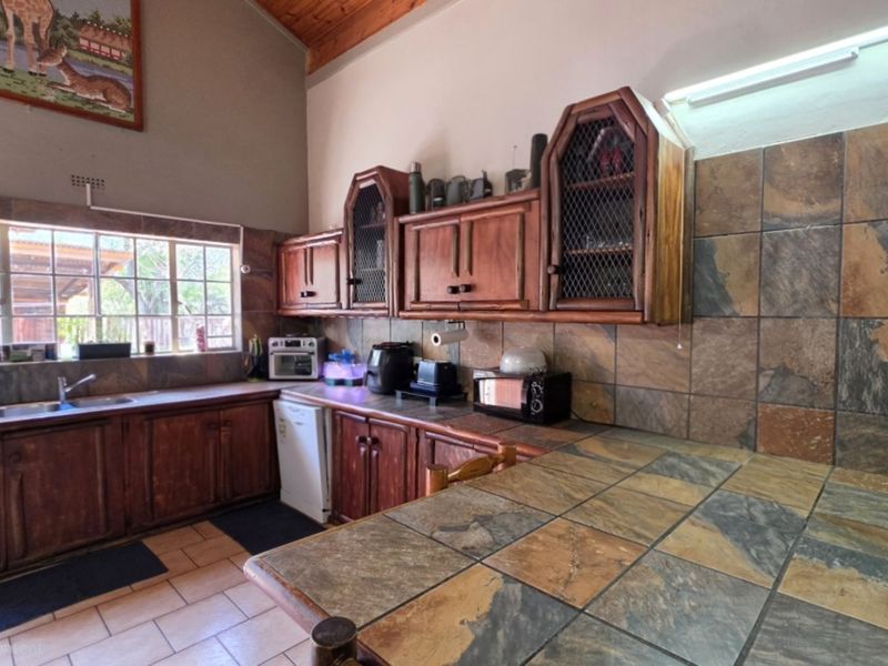 A rustic kitchen featuring wooden cabinetry, slate tile countertops and backsplash, and exposed timber ceiling beams, offering a traditional aesthetic.