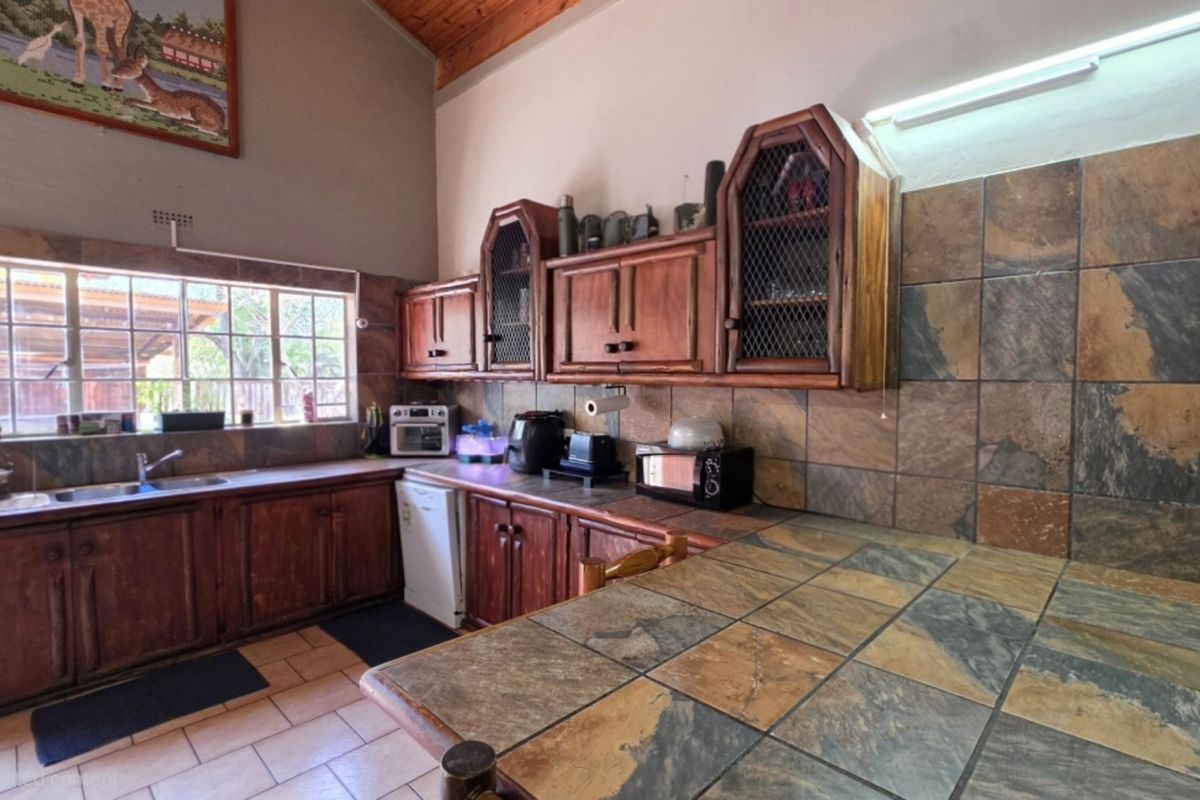 A rustic kitchen featuring wooden cabinetry, slate tile countertops and backsplash, and exposed timber ceiling beams, offering a traditional aesthetic.