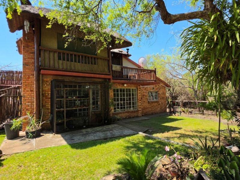 Rear view of a double-story house featuring exposed brick walls, a thatched roof, and a wooden balcony overlooking a private garden.