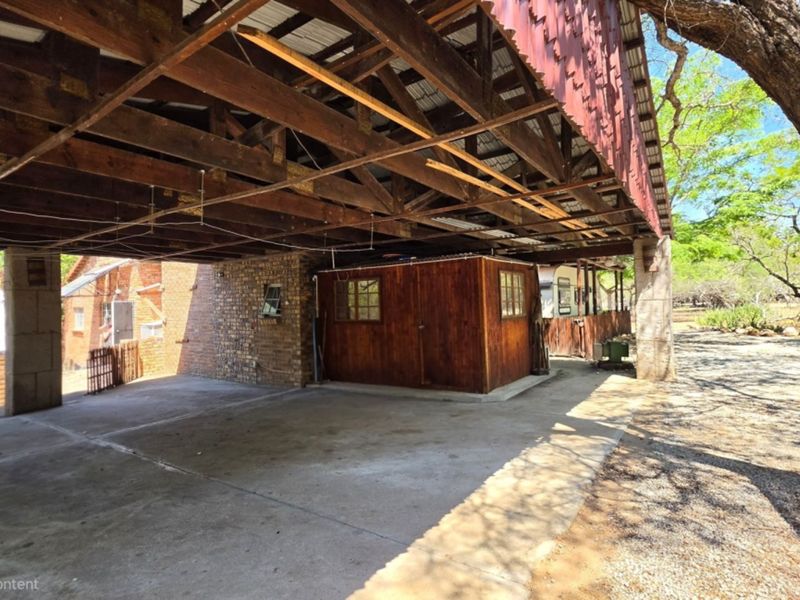 A large covered outdoor patio area featuring exposed timber roof trusses, concrete flooring, and brick masonry, suitable for renovation or outdoor living space development.