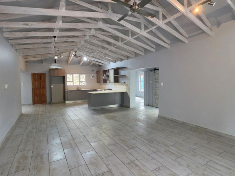 Spacious open-plan living and kitchen area featuring high vaulted ceilings with exposed timber trusses, modern tiled flooring, and a functional kitchen island.
