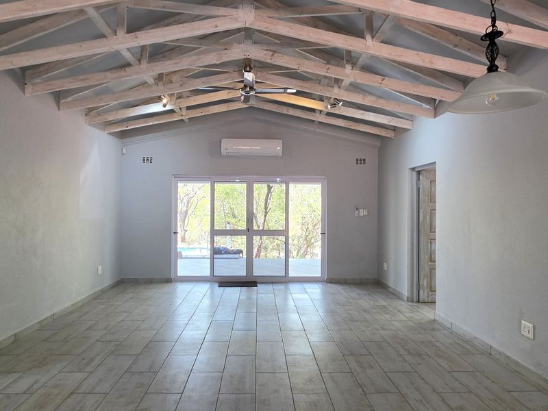 Spacious living area featuring high vaulted ceilings with exposed timber trusses, tiled flooring, and large sliding glass doors leading to the outdoors.