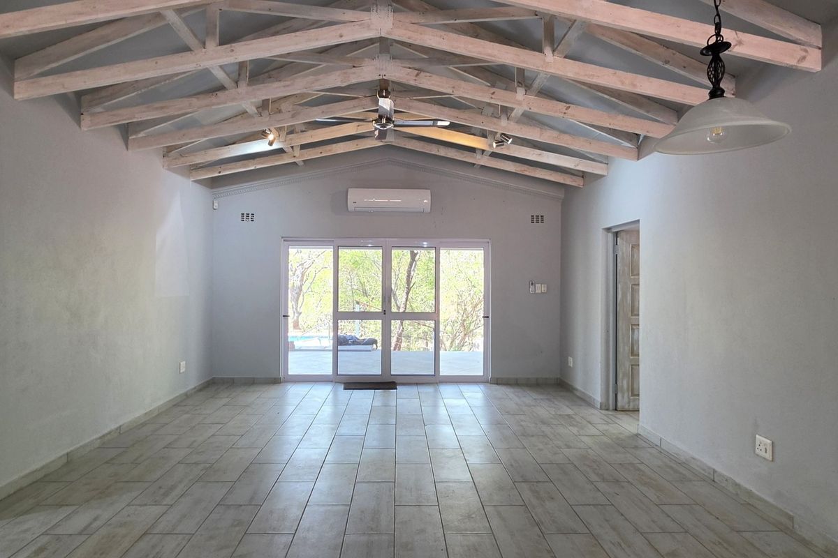 Spacious living area featuring high vaulted ceilings with exposed timber trusses, tiled flooring, and large sliding glass doors leading to the outdoors.