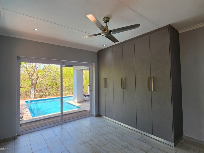 Modern bedroom featuring built-in cupboards, tiled flooring, and a sliding glass door providing direct access to the outdoor pool area.