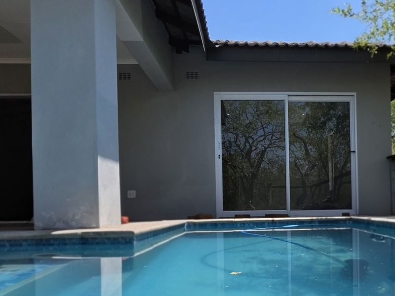 A view of a swimming pool adjacent to a covered patio area with sliding glass doors leading into the home.
