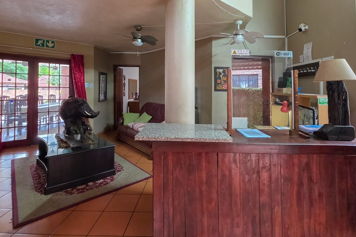 A spacious living area featuring tiled floors, ceiling fans, and a built-in reception counter with a glass partition, leading out to a patio.
