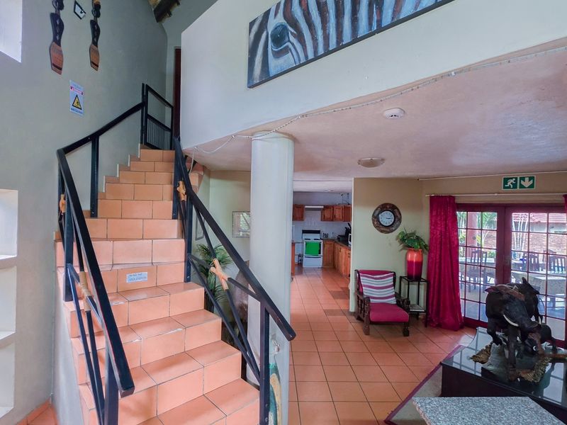 Open plan living area featuring tiled flooring, a central structural column, a staircase with metal railings, and a view through to the kitchen area.